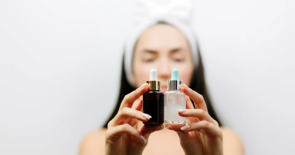 Dłonie trzymające dwie buteleczki serum z pipetą na jasnym tle
